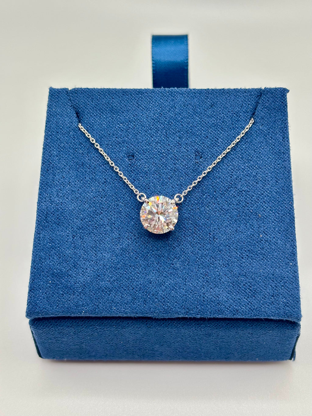 Round brilliant 2 carat lab diamond solitaire necklace in white gold, close-up on blue box