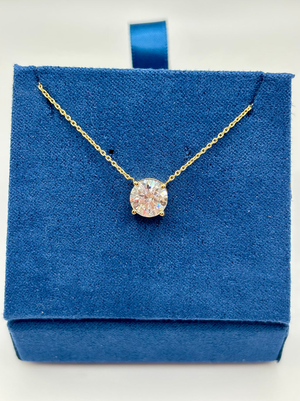 Pink lab diamond solitaire necklace on blue jewelry box, close-up